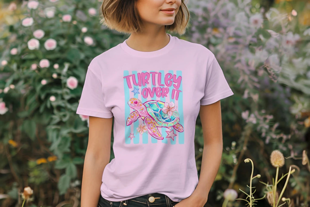 Person wearing a light purple t-shirt with a colorful turtle graphic and text, standing in a garden.